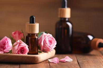 Bottles of essential rose oil and flowers on wooden table