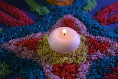 Photo of Diwali celebration. Burning candle and colorful rangoli on table, closeup