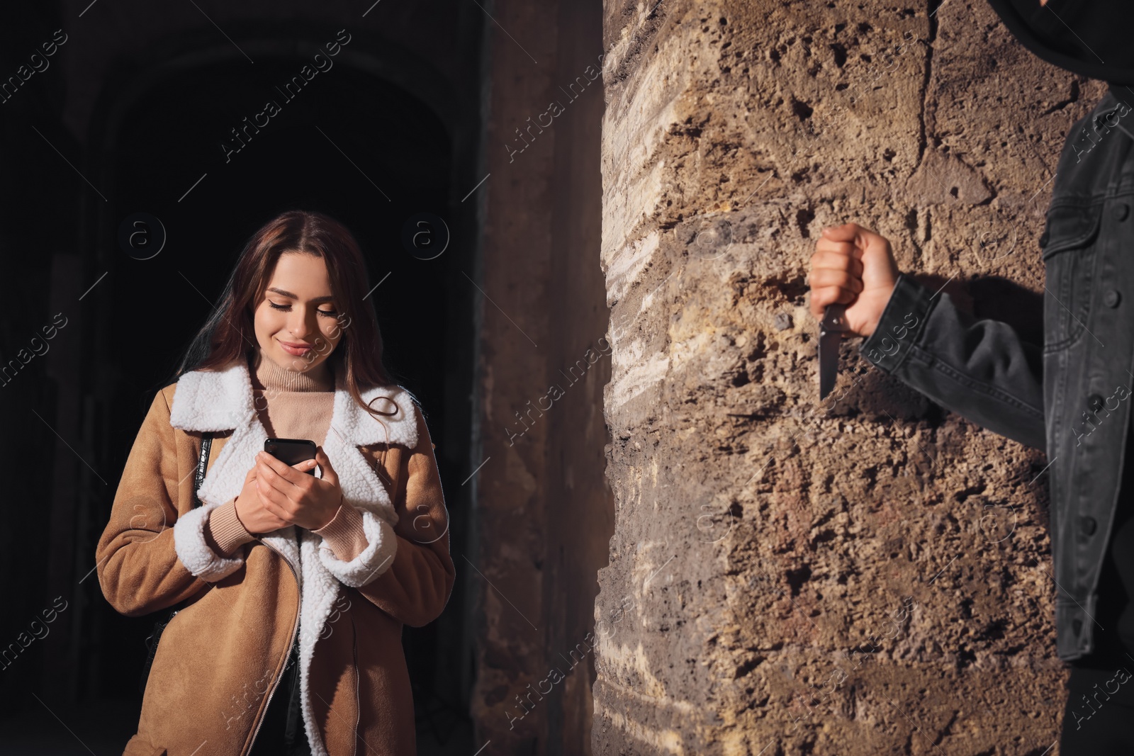 Photo of Criminal with knife hiding behind wall and waiting for victim near alley at night