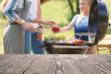 Image of Empty wooden table and blurred view of family having barbecue with modern grill outdoors