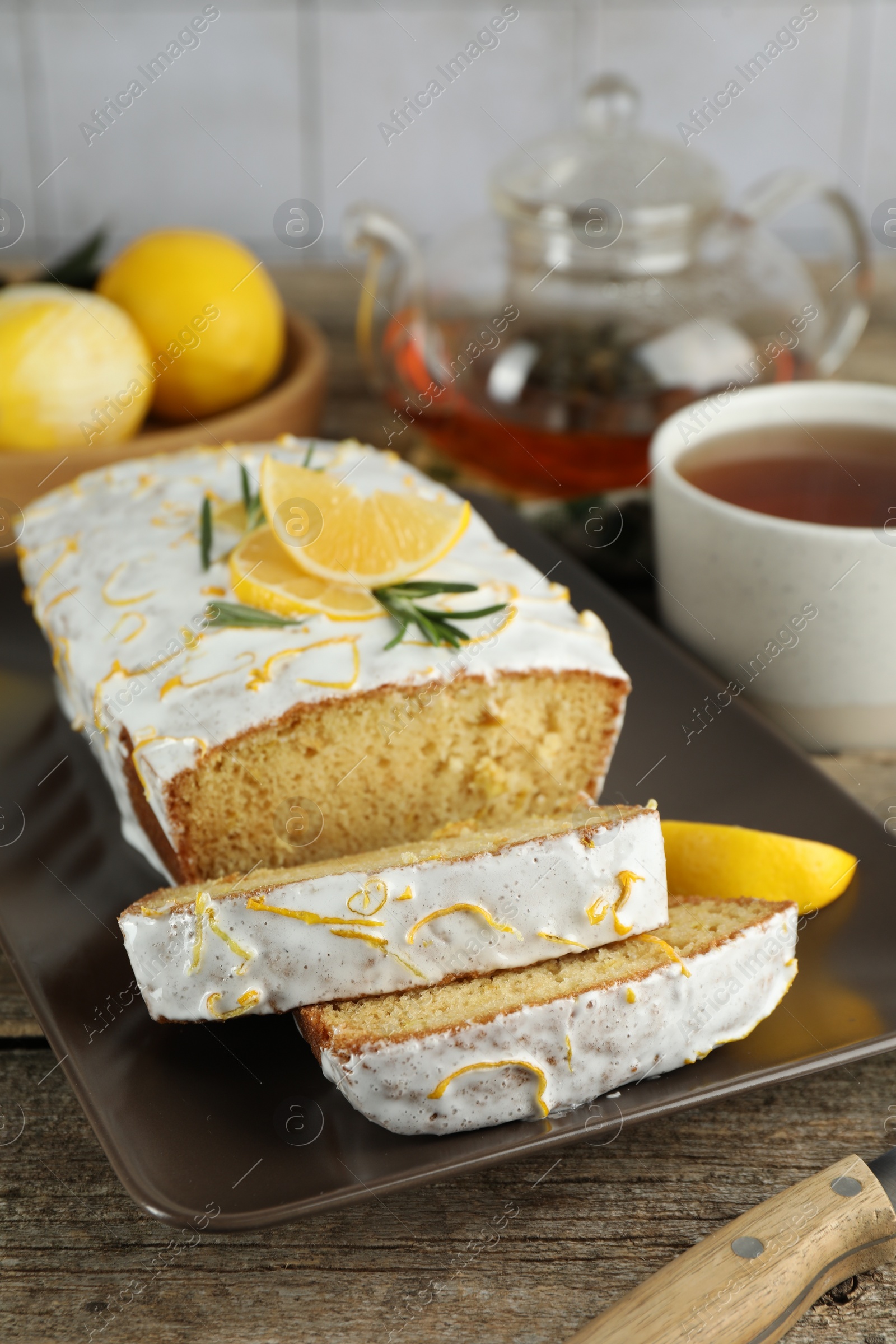 Photo of Tasty lemon cake with glaze and tea on wooden table, closeup