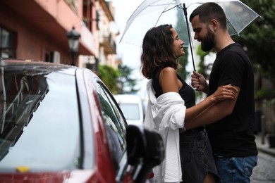 Young couple with umbrella enjoying time together under rain on city street, space for text