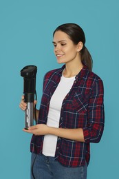 Photo of Beautiful young woman holding sous vide cooker on light blue background