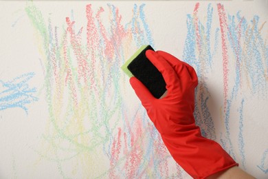 Photo of Woman erasing child's drawing from white wall, closeup