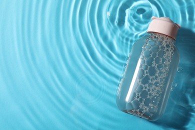 Photo of Bottle of micellar water in liquid on light blue background, top view. Space for text