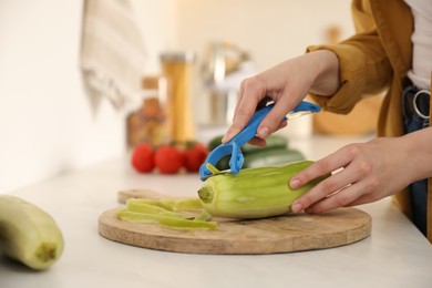 Photo of Woman peeling zucchini at kitchen counter, closeup. Preparing vegetable