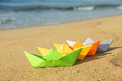 Photo of Bright colorful paper boats on sandy beach near sea