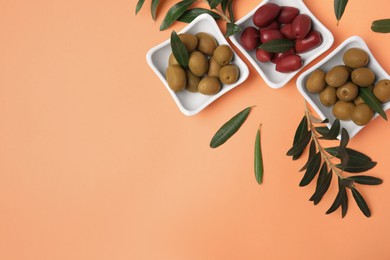 Photo of Different fresh olives and green leaves on pale orange background, flat lay. Space for text