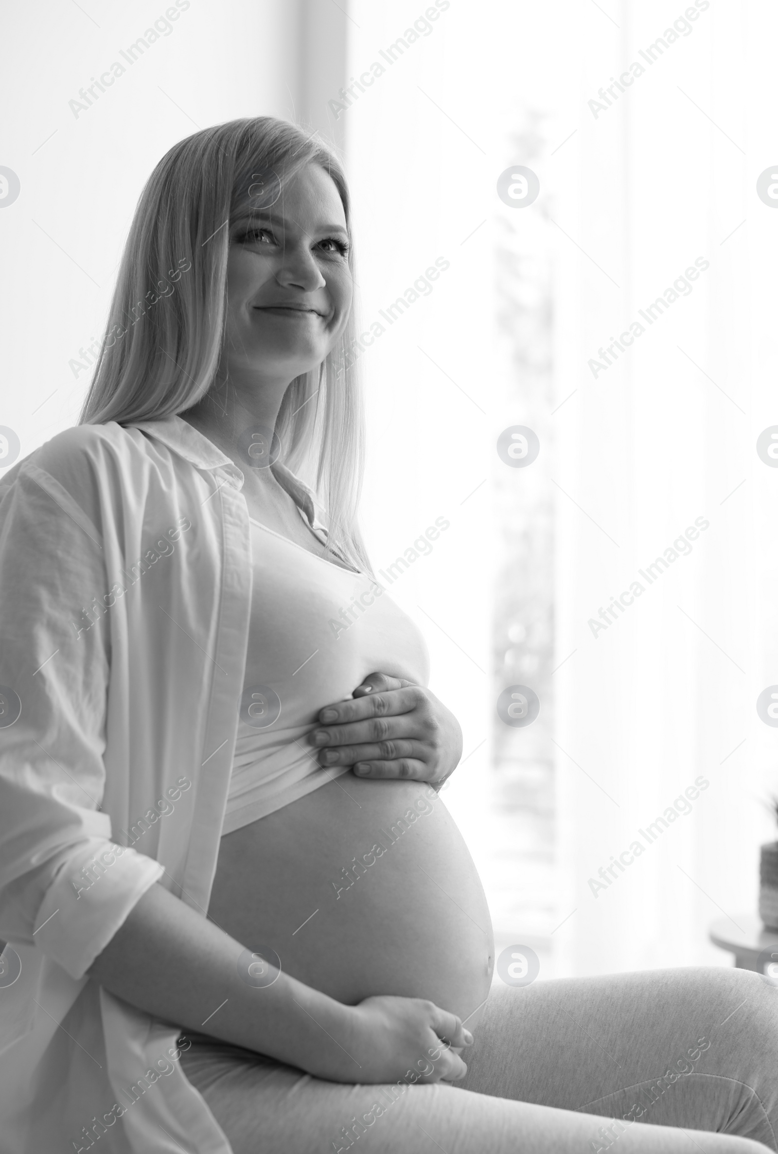 Photo of Beautiful pregnant woman sitting in light room at home, black and white effect