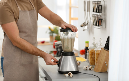 Young man using blender to cook cream soup in kitchen, closeup