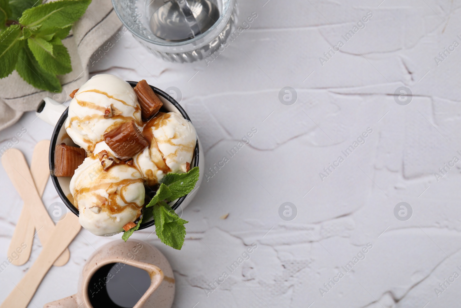 Photo of Scoops of ice cream with caramel sauce, candies and mint leaves on white textured table, flat lay. Space for text