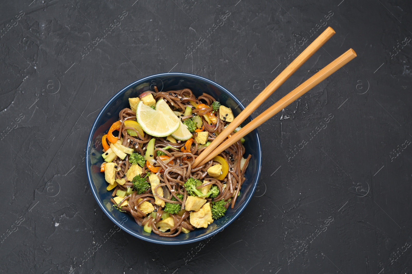 Photo of Stir-fry. Delicious cooked noodles with chicken and vegetables in bowl served on gray textured table, top view