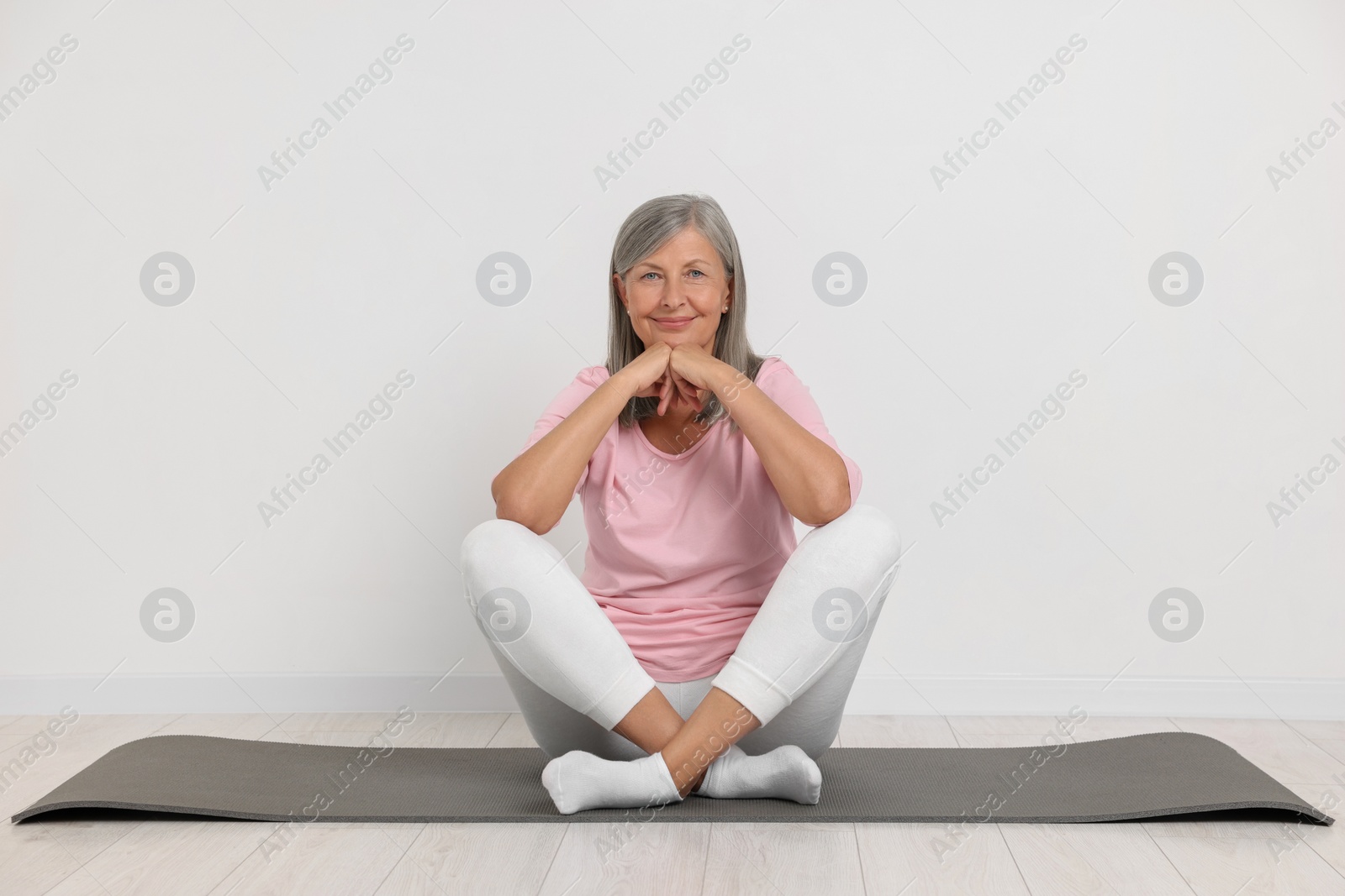 Photo of Happy senior woman sitting on mat near white wall. Yoga practice