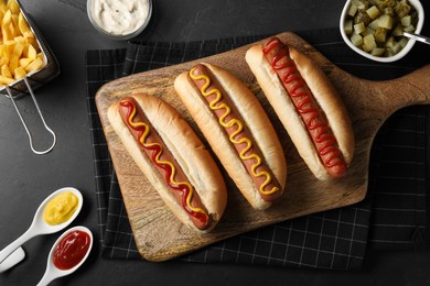 Fresh delicious hot dogs and ingredients on black table, flat lay