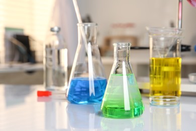 Photo of Laboratory analysis. Glassware with different liquids on white table indoors, closeup