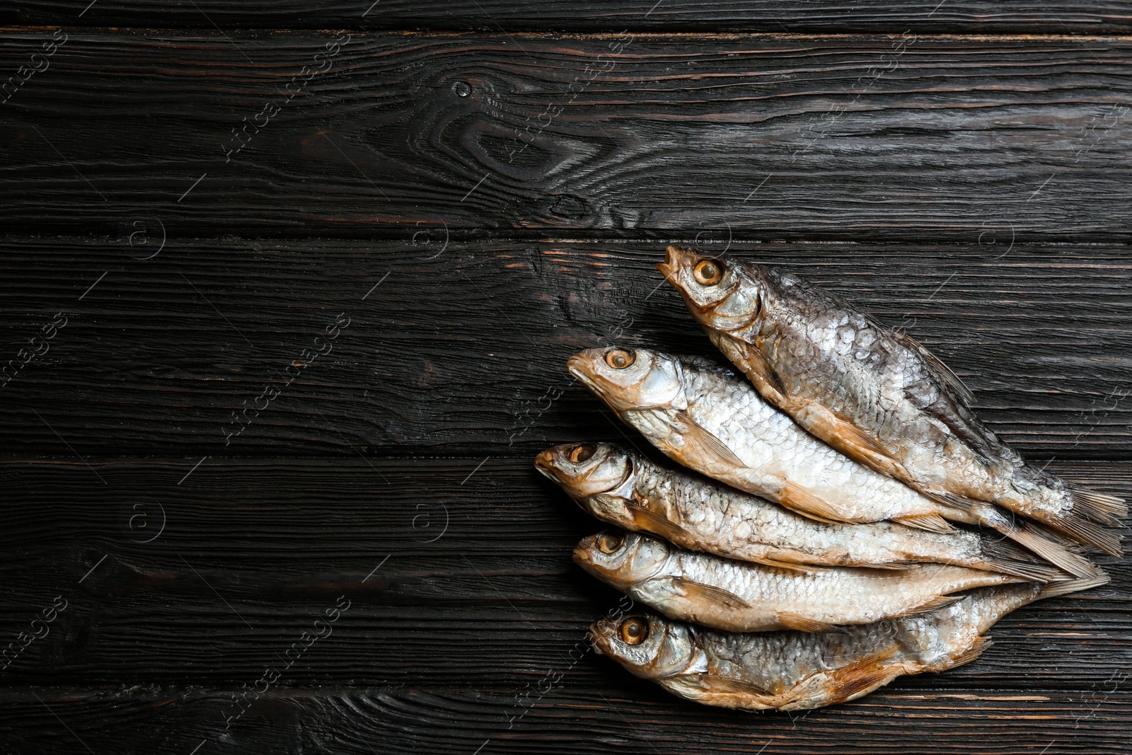 Photo of Tasty dried fish on black wooden table, flat lay. Space for text