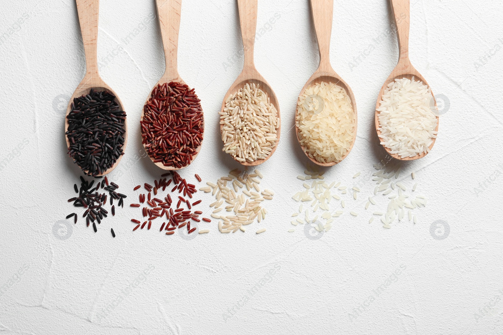 Photo of Flat lay composition with brown and other types of rice in spoons on white background. Space for text