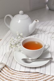 White teapot with saucer and cup of tea on countertop in kitchen