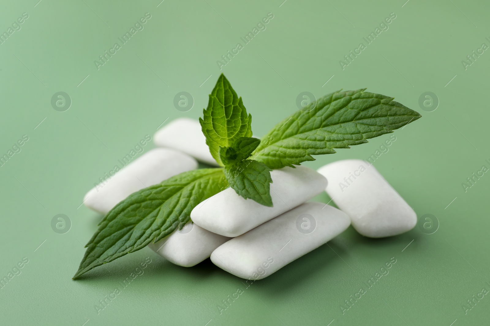 Photo of Tasty white chewing gums and mint leaves on light green background, closeup