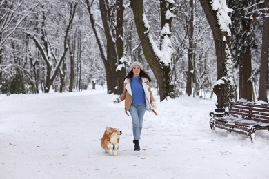 Woman with adorable Pembroke Welsh Corgi dog running in snowy park