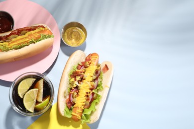 Photo of Delicious hot dogs with bacon, lettuce, onion and pickle served on light blue table, flat lay. Space for text