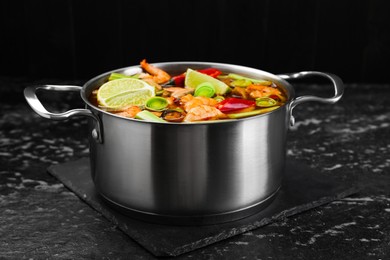 Photo of Saucepan with delicious Tom Yum soup on black marble table