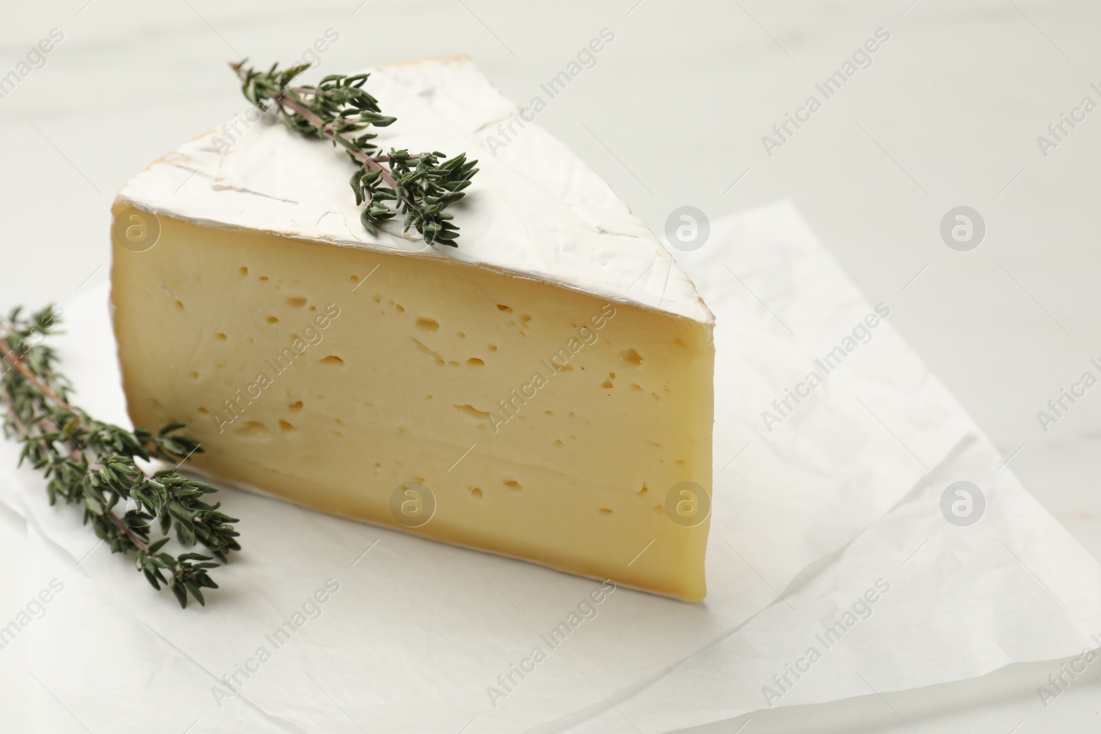 Photo of Piece of tasty camembert cheese and thyme on white table, closeup