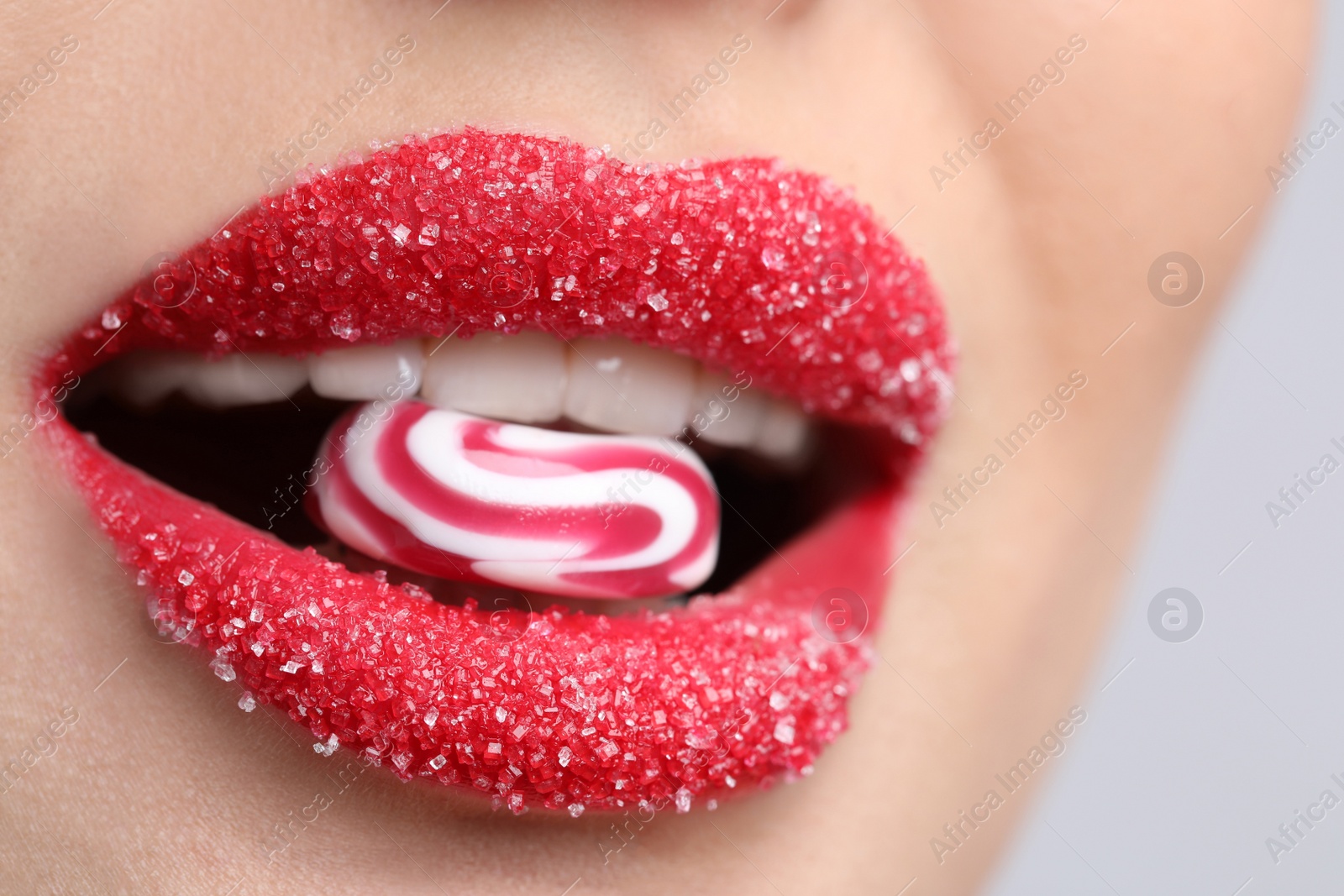 Photo of Young woman with beautiful lips covered in sugar eating candy on light background, closeup