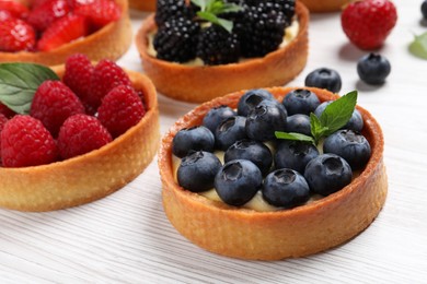 Photo of Tartlets with different fresh berries on white wooden table, closeup. Delicious dessert