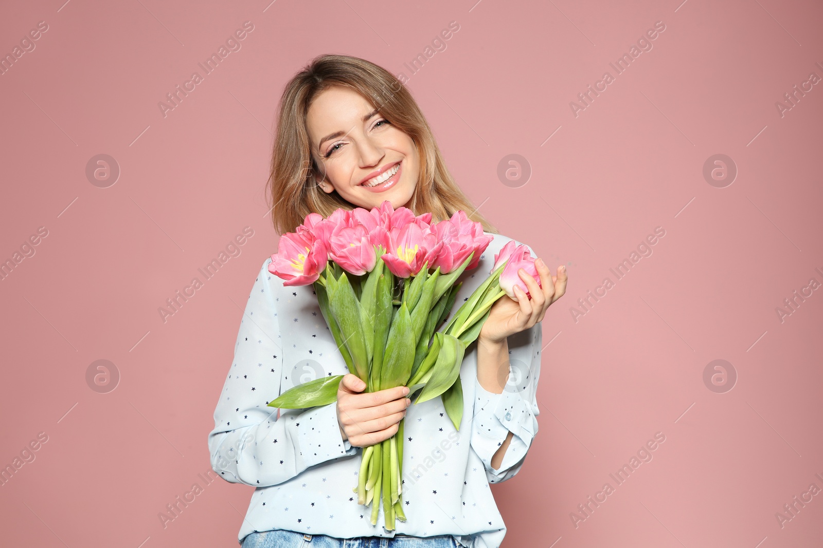 Photo of Portrait of beautiful smiling girl with spring tulips on pink background. International Women's Day