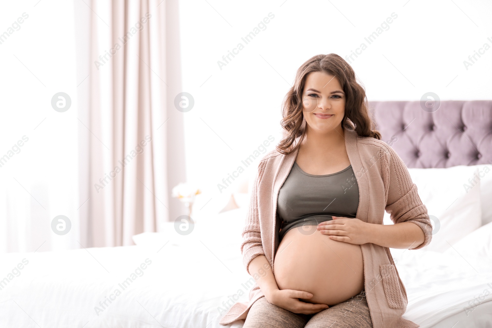 Photo of Young pregnant woman sitting on bed at home