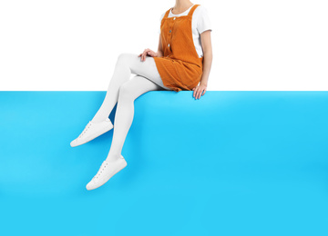 Photo of Woman wearing white tights and stylish shoes sitting on color background, closeup