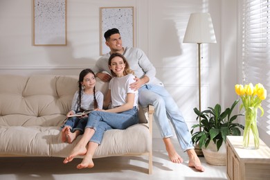Photo of Happy family with little daughter sitting on sofa at home
