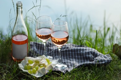 Photo of Delicious rose wine, cheese and grapes on picnic blanket near lake, closeup