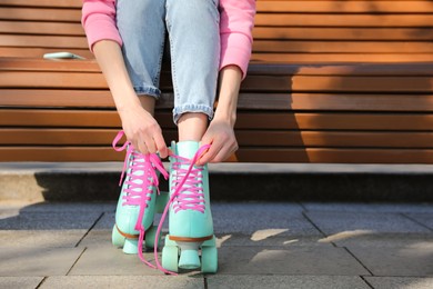Photo of Woman lacing roller skates while sitting on bench outdoors, closeup