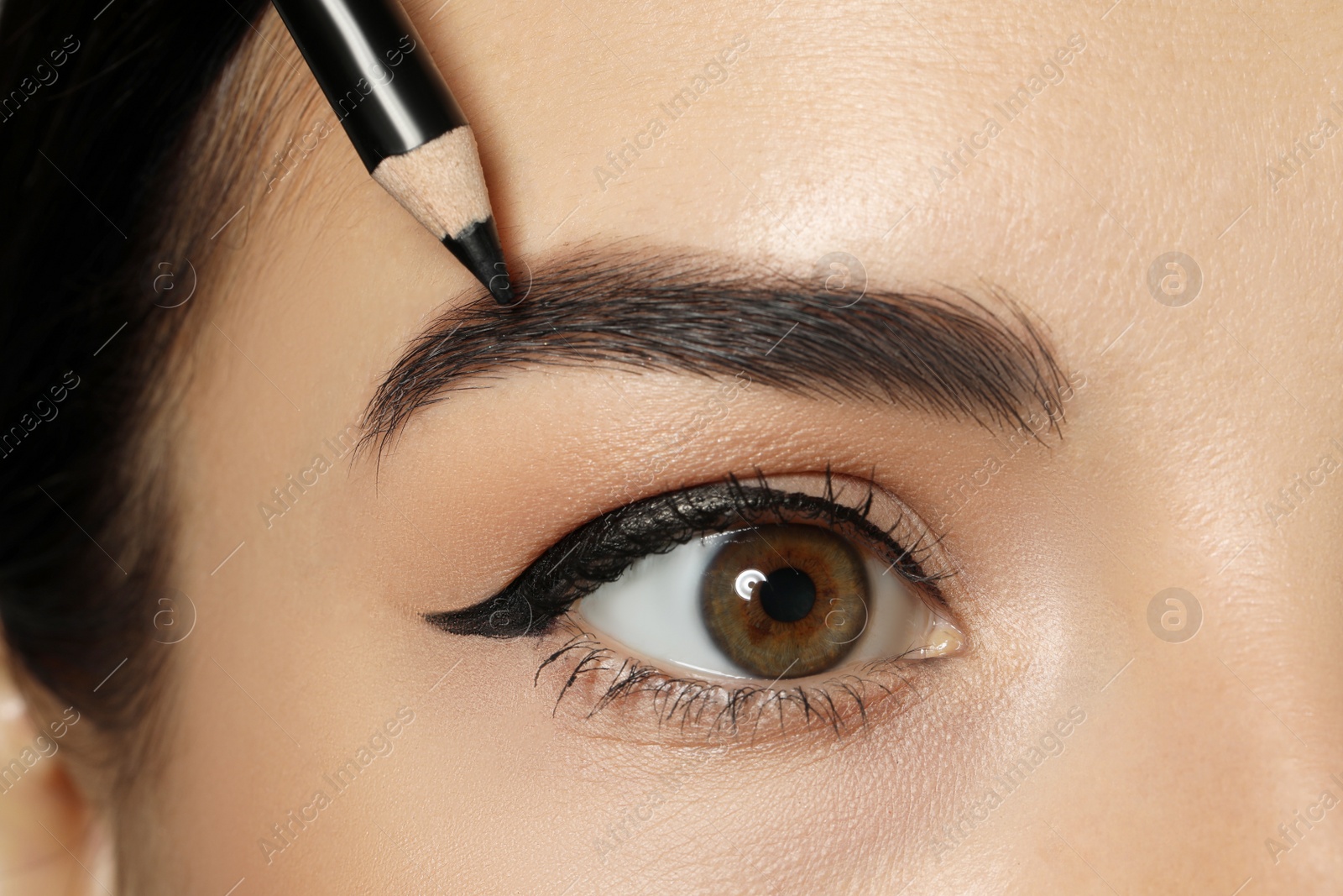 Photo of Young woman correcting eyebrow shape with pencil, closeup view