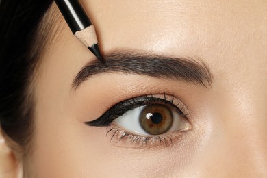 Young woman correcting eyebrow shape with pencil, closeup view