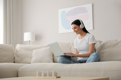 Photo of Woman with laptop and headphones sitting on sofa at home