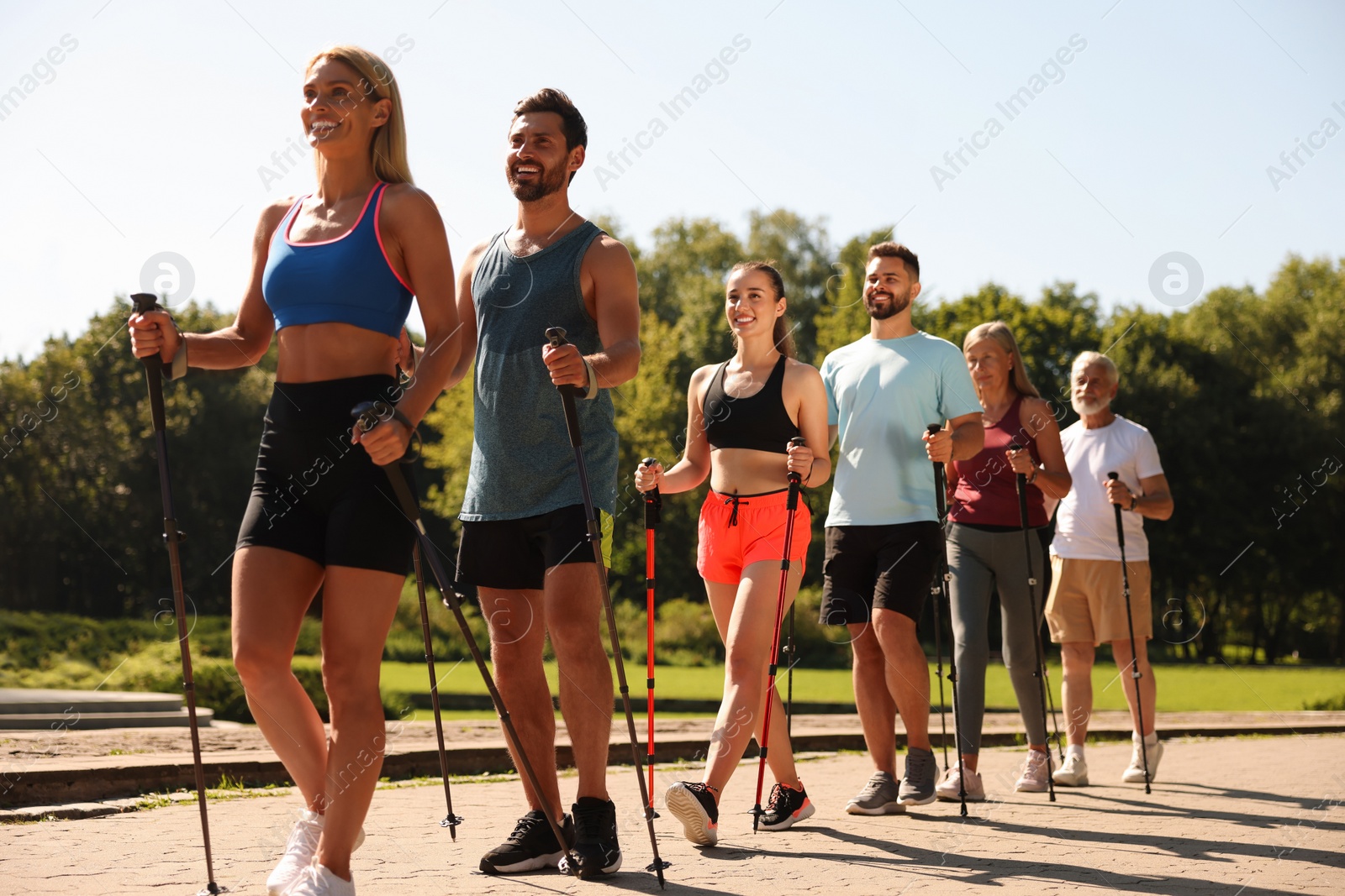 Photo of Group of people practicing Nordic walking with poles in park on sunny day