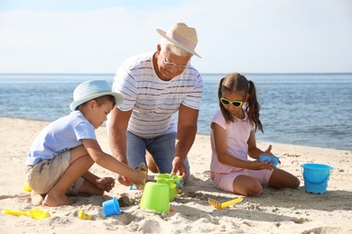 Photo of Little children and grandfather playing with plastic toys on sea beach