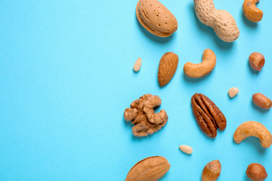 Different delicious nuts on light blue background, flat lay. Space for text