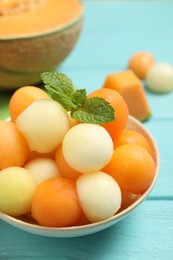 Photo of Melon balls and mint in bowl on light blue table, closeup