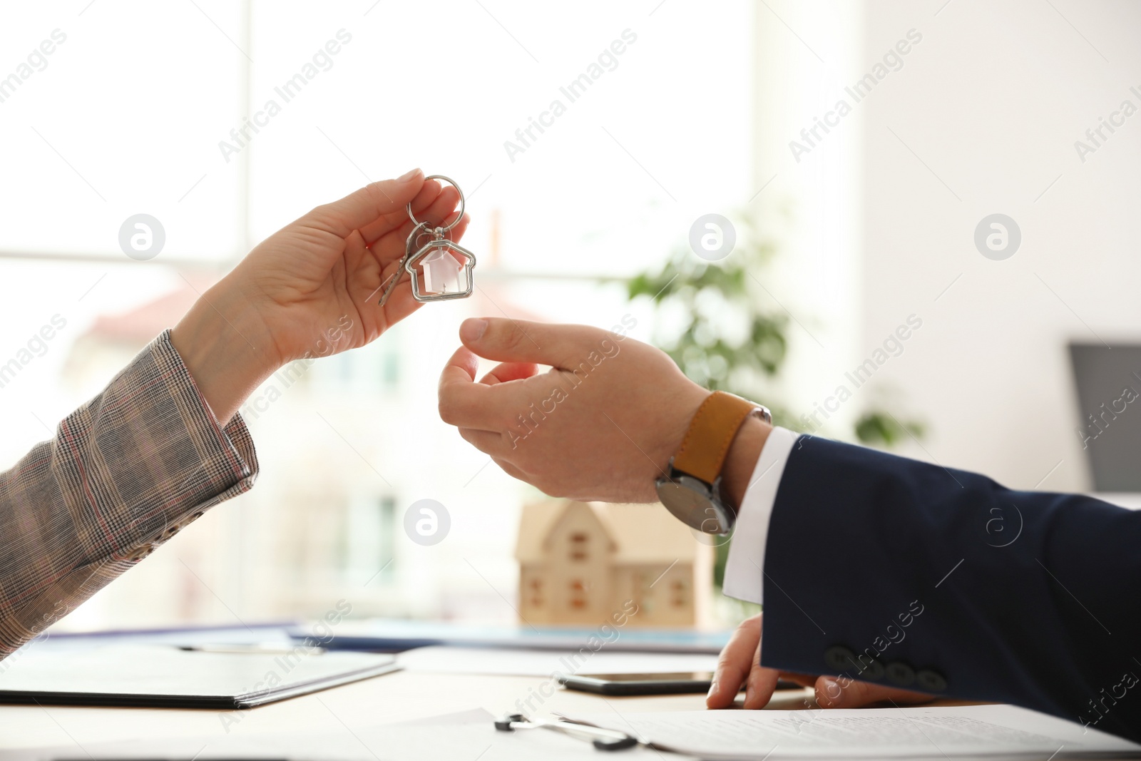 Photo of Real estate agent giving key with trinket to client in office, closeup