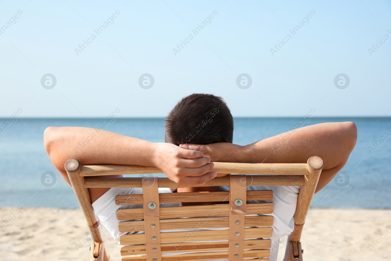 Photo of Young man relaxing in deck chair on sandy beach