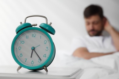 Photo of Sleepy man awaking at home in morning, focus on alarm clock. Space for text