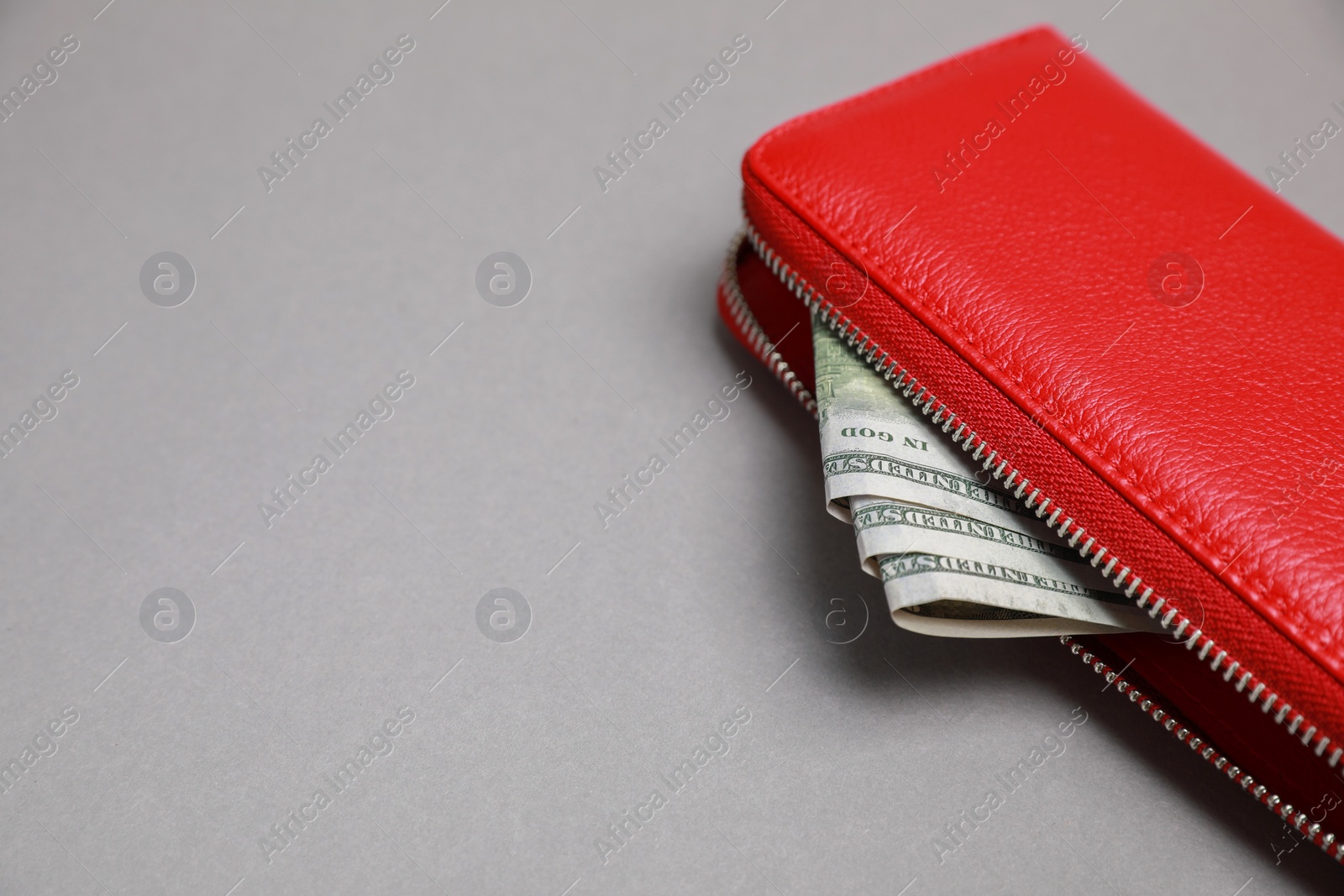 Photo of Stylish red leather purse with dollar banknotes on light grey background, closeup. Space for text