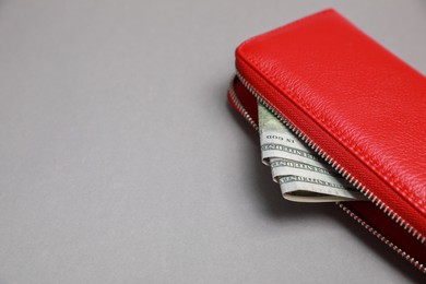 Photo of Stylish red leather purse with dollar banknotes on light grey background, closeup. Space for text