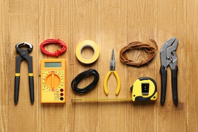 Photo of Wires and electrician's tools on wooden table, flat lay