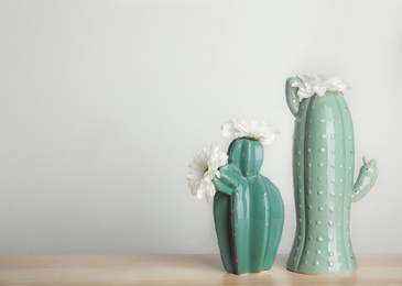 Photo of Trendy cactus shaped vases with flowers on table against light wall. Creative decor