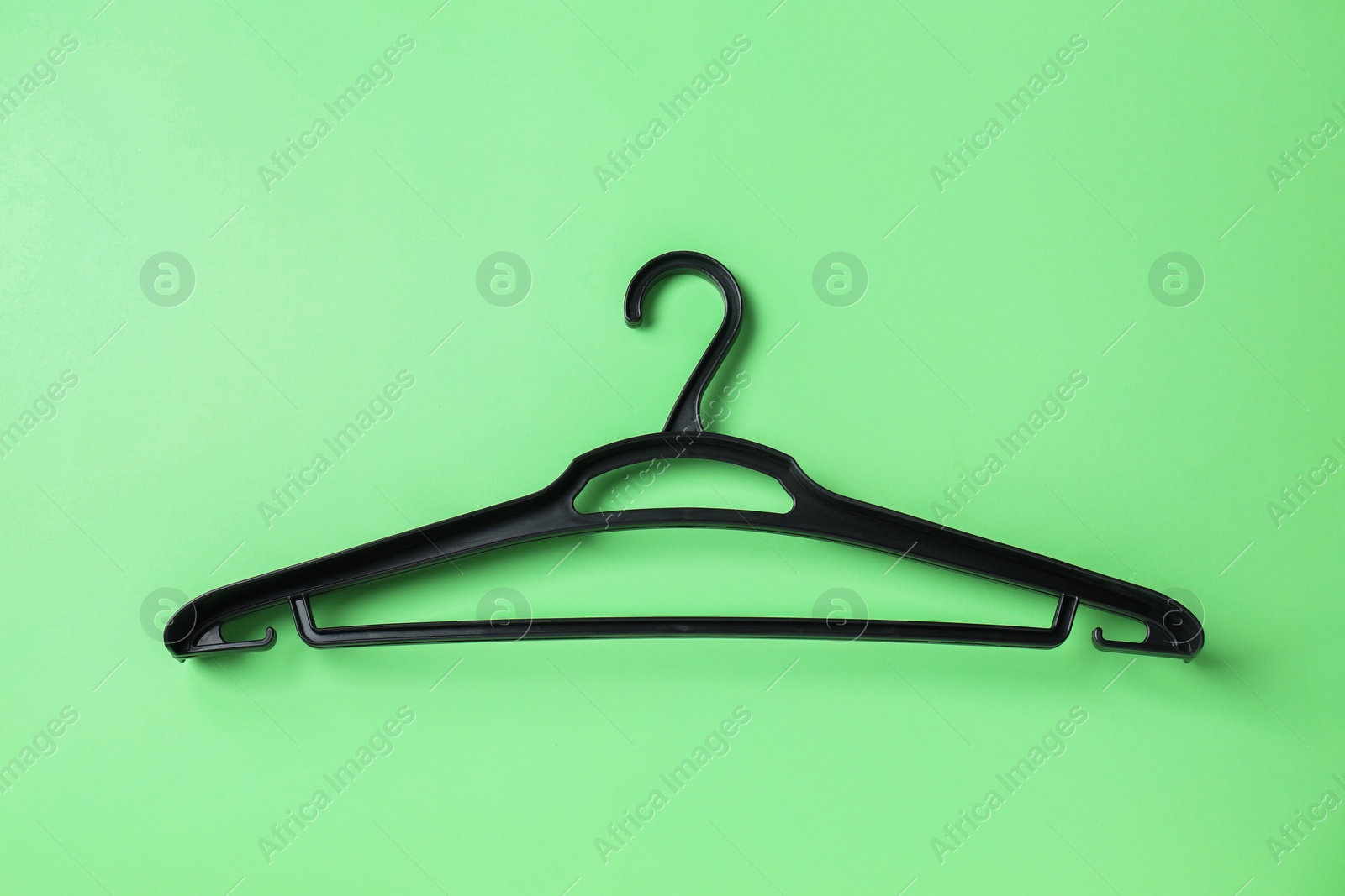 Photo of Empty black hanger on light green background, top view